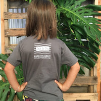 girl with hands on hips in front of monstera leaves wearing a green tshirt with a white postage stamp logo